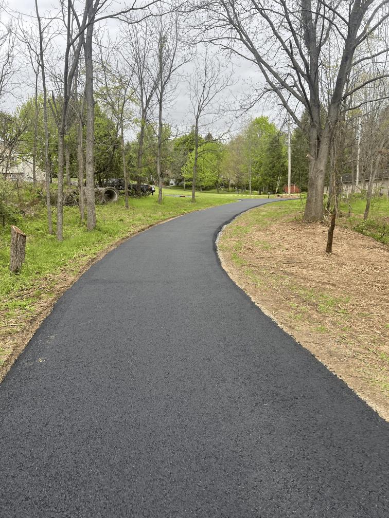Newly paved asphalt driveway alongside a two-story tan-sided home by R. Stanley's Paving.
