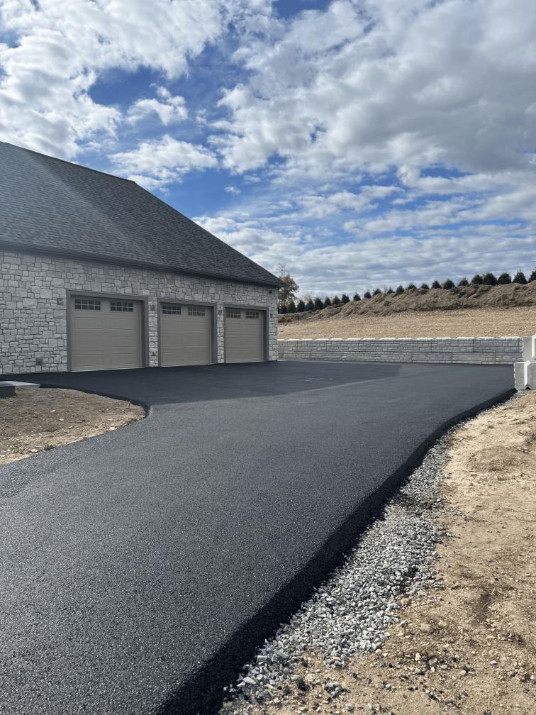 Wide new asphalt driveway at a three-car garage on a stone home by R. Stanley's Paving.