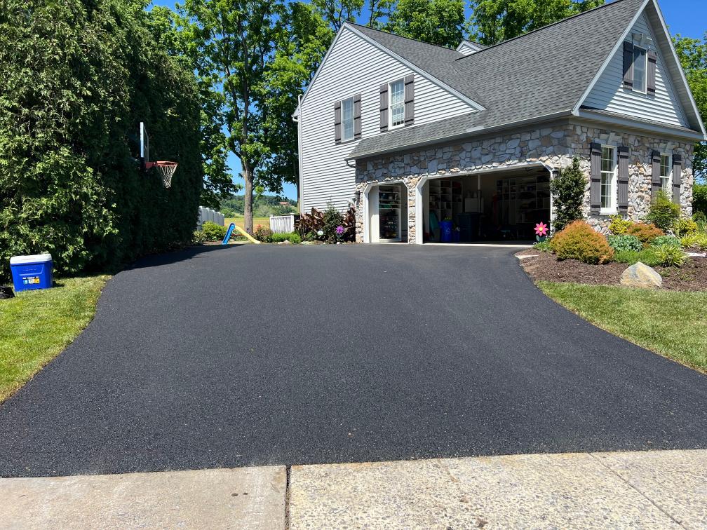 New asphalt driveway with a basketball hoop at a stone and vinyl home by R. Stanley's Paving.