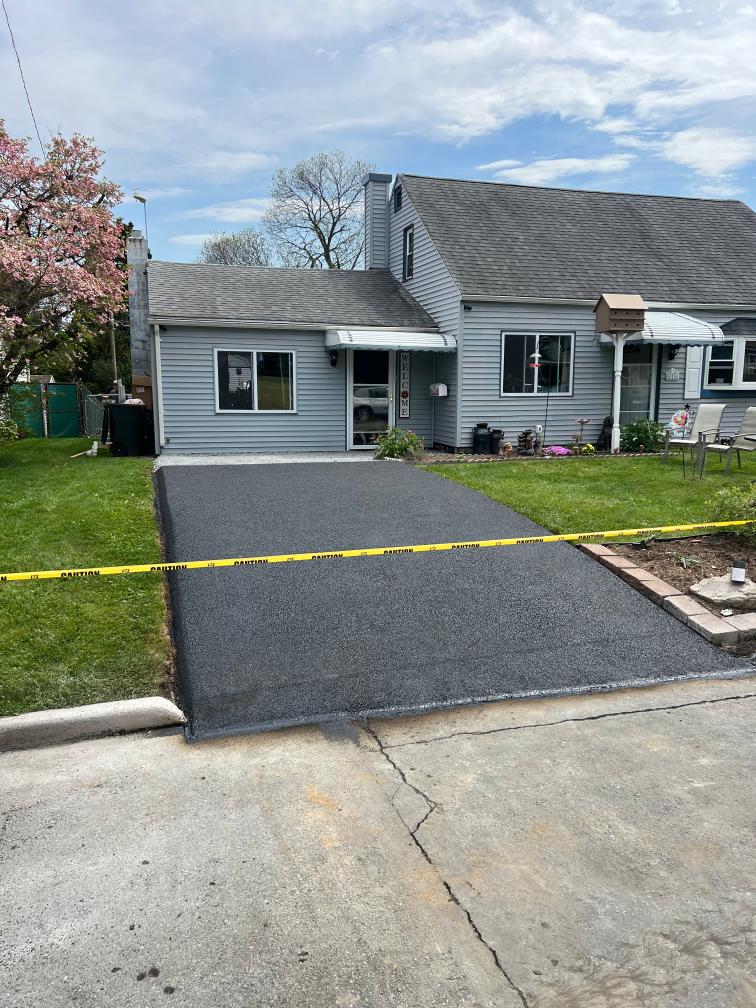After: freshly paved asphalt driveway in front of a gray Cape Cod home.