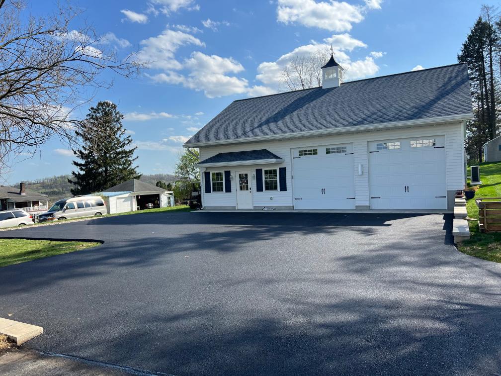 New asphalt driveway leading to a white two-story garage with a cupola by R. Stanley's Paving.