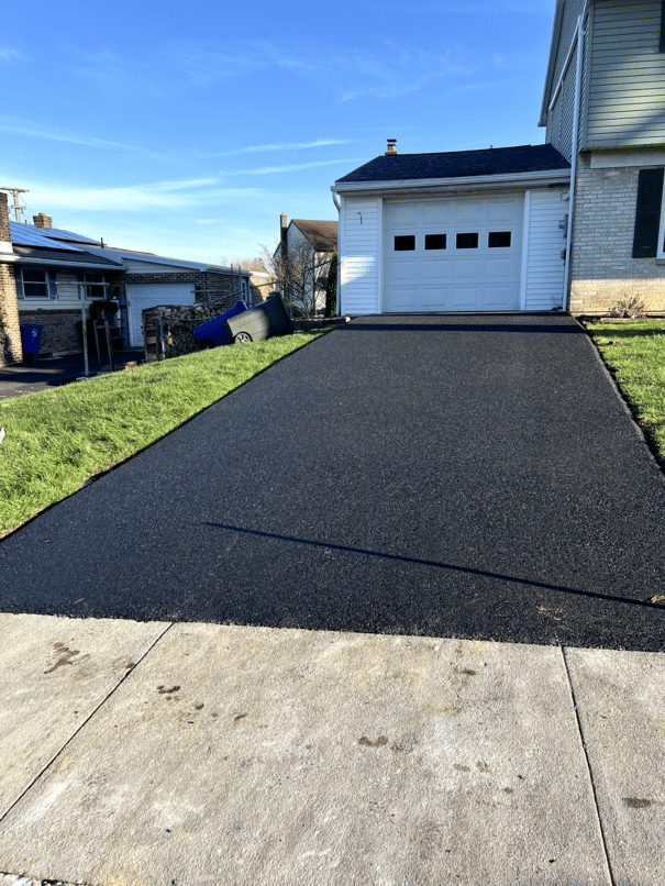 Freshly paved asphalt driveway leading to a white single-car garage in the Leesport area by R. Stanley's Paving.